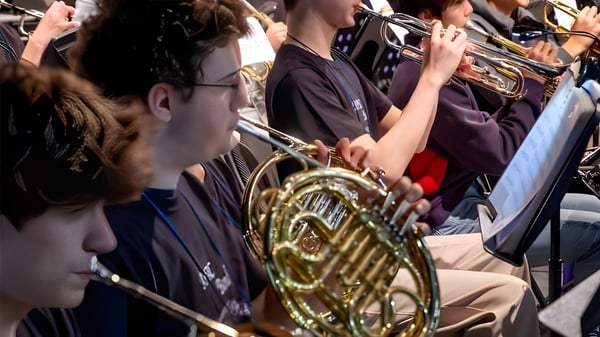 Eine Gruppe von Musikern in den maronen Uniformen der Taejon Christian International School spielt Blechblasinstrumente während einer Aufführung.