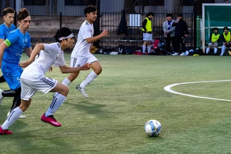 Schüler der Taejon Christian International School spielen Fußball auf dem Sportplatz mit Zuschauern im Hintergrund.