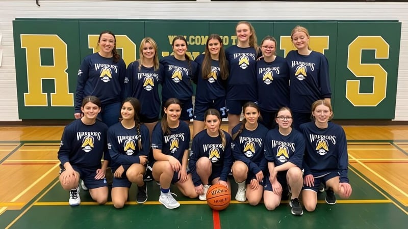 Eine Gruppe junger Basketballspielerinnen posiert in der Sporthalle der Tagwi Secondary School vor dem großen RAMS-Logo an der Wand.
