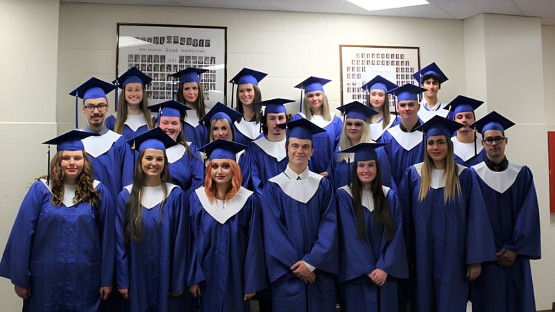 Eine Gruppe von Absolventen der Tagwi Secondary School trägt blaue Abschlussroben und steht gemeinsam in einem Klassenraum.