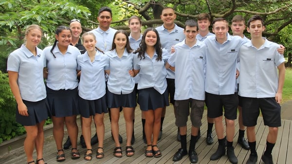 Eine Gruppe Schülerinnen und Schüler in Schuluniformen steht zusammen im grünen Außenbereich des Tauhara College.