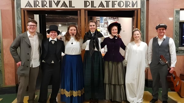 Eine Gruppe von Schülern der Taieri College steht vor dem Schild 'Ankunftsplattform' an einem Bahnhof.