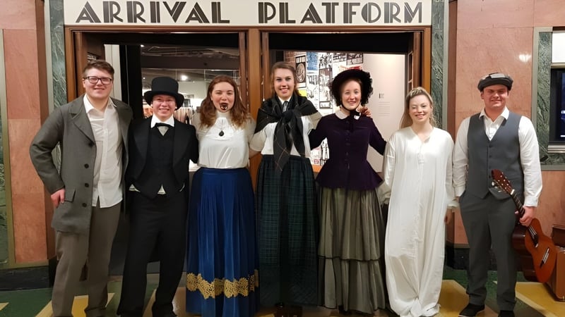 Eine Gruppe von Schülern der Taieri College steht vor dem Schild 'Ankunftsplattform' an einem Bahnhof.