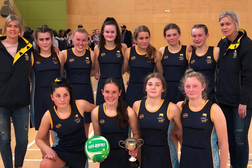 Eine Gruppe junger Athletinnen des Taieri College hält in der Sporthalle einen Pokal.