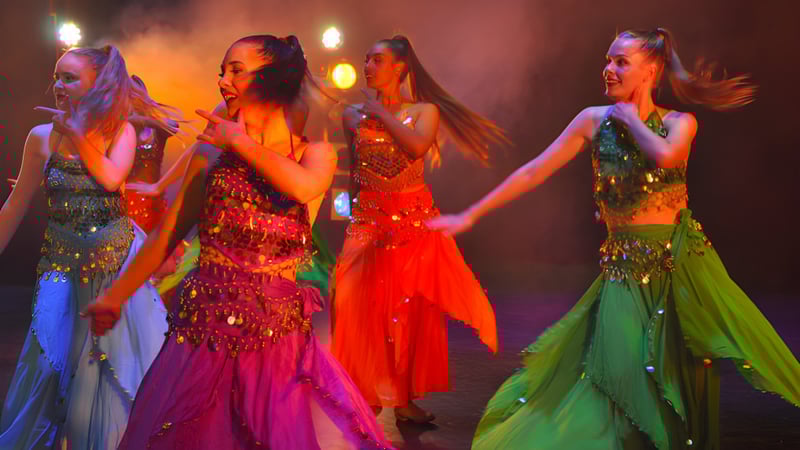 Vier Schülerinnen der Takapuna Grammar School führen auf einer Bühne mit dramatischer Beleuchtung einen Auftritt in farbenfrohen Kleidern auf.