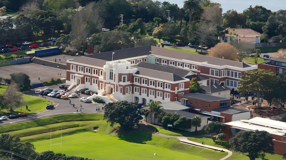 Das mehrstöckige Backsteingebäude der Takapuna Grammar School steht auf einem grasbewachsenen Hügel umgeben von Bäumen.