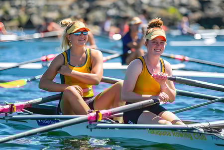 Zwei Schülerinnen der Takapuna Grammar School sitzen in einem kleinen Ruderboot auf dem Wasser vor Zuschauern.