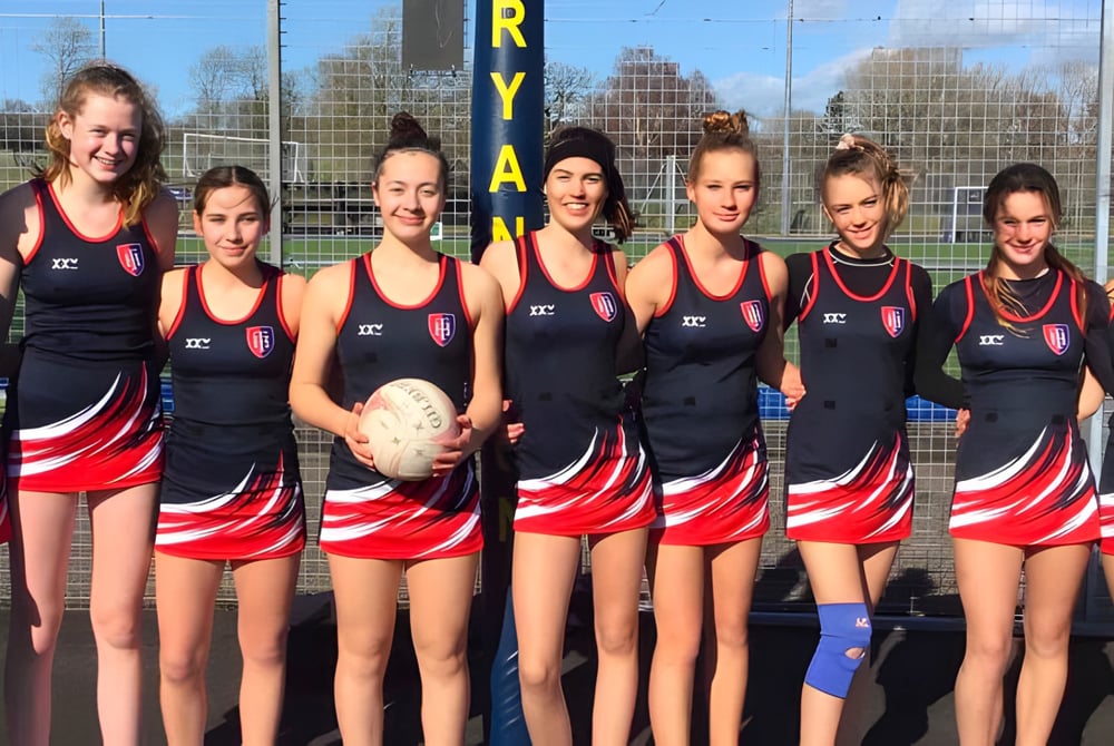 Eine Gruppe junger Sportlerinnen der Talbot Heath School steht mit einem Rugbyball auf dem Sportplatz.
