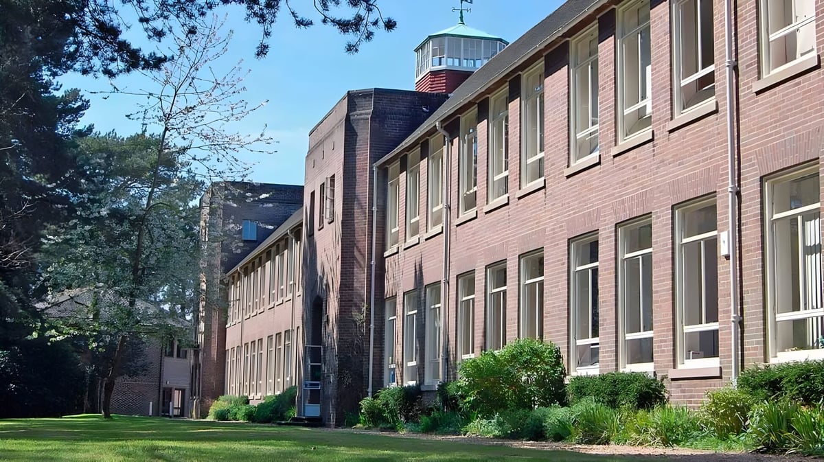 Das mehrstöckige Backsteingebäude mit grünem Dach der Talbot Heath School ist von Bäumen und gepflegten Grünflächen umgeben.