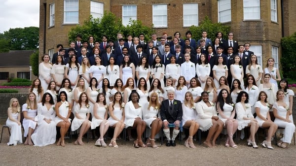Eine Gruppe von Menschen in formeller Kleidung posiert vor einem historischen Gebäude auf dem Campus der TASIS The American International School in England.