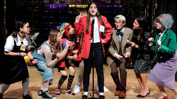 Eine Gruppe von Schülerinnen und Schülern der TASIS The American International School in England steht auf einer Bühne vor einem neonbeleuchteten Hintergrund.