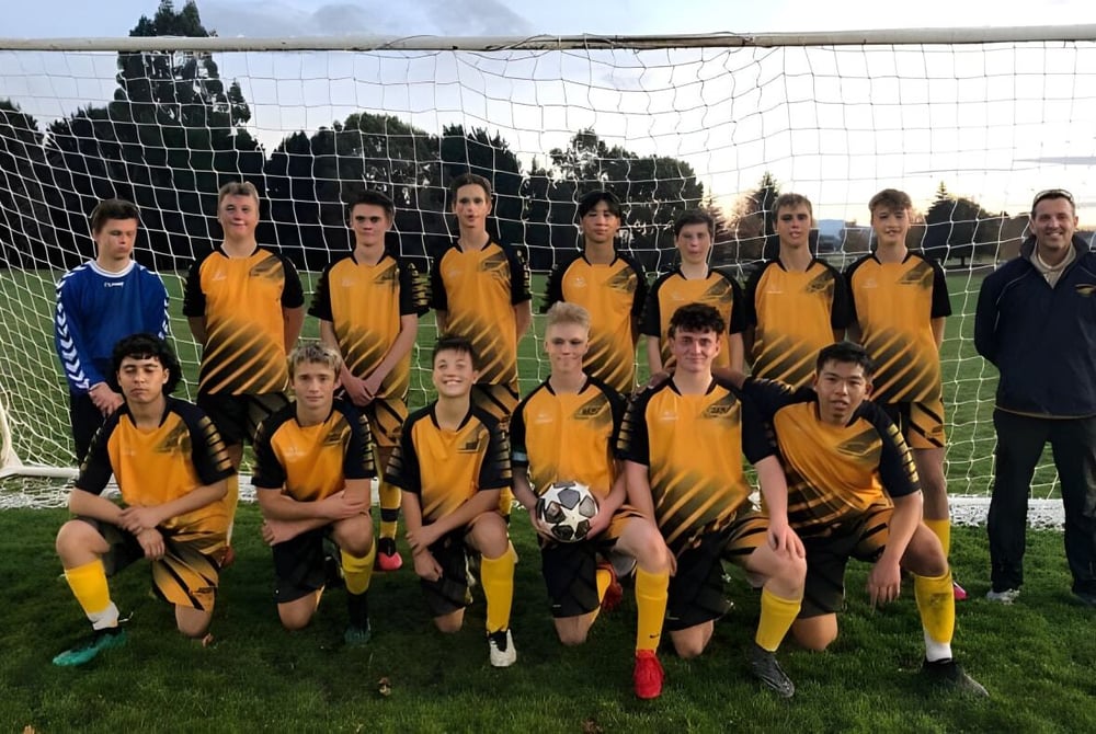Eine Gruppe von Schülerinnen und Schülern posiert als Fußballmannschaft auf dem Spielfeld des Tauhara College.