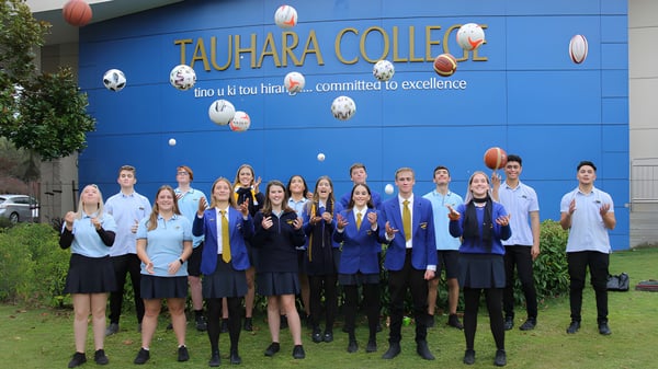 Eine Gruppe Schüler in Schuluniformen steht vor der blauen Wand mit dem Logo von Tauhara College.