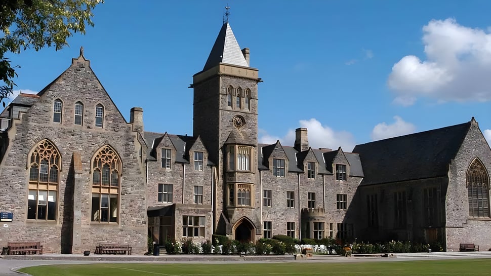 Das mittelalterliche Steingebäude der Taunton School International ist von grüner Umgebung umgeben und zeigt Menschen im Vordergrund.