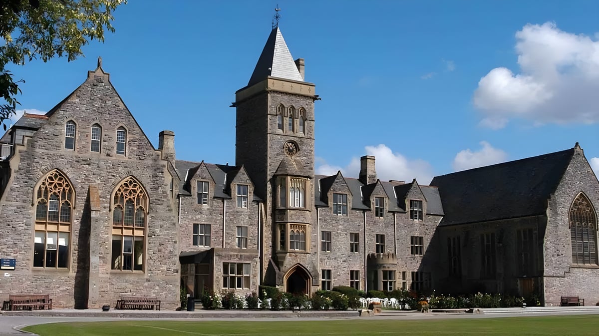 Das mittelalterliche Steingebäude der Taunton School International ist von grüner Umgebung umgeben und zeigt Menschen im Vordergrund.