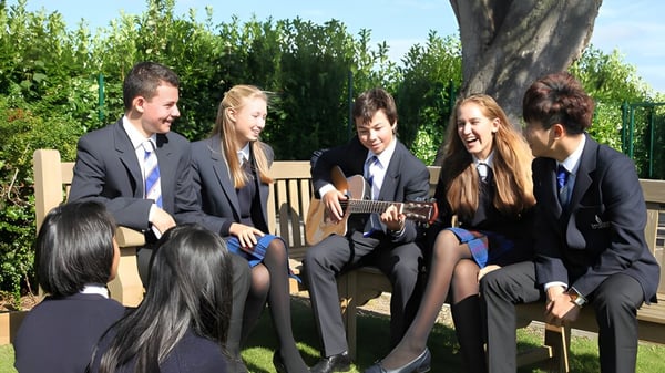 Schüler der Taunton School International sprechen in formeller Kleidung im Freien mit grüner Vegetation im Hintergrund.