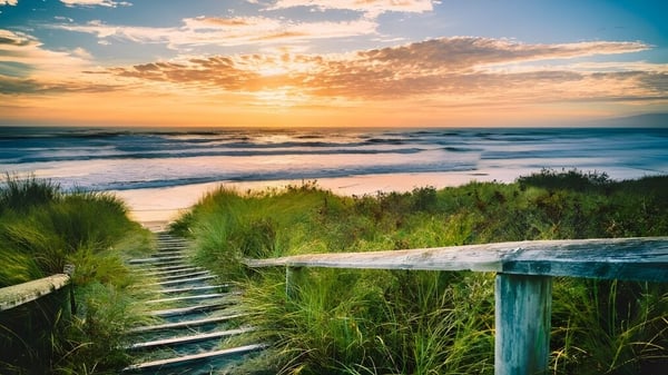 Ein Strand mit einer Holztreppe zum Meer bei Sonnenuntergang zeigt eine Szene nahe dem Tauranga Boy's College.