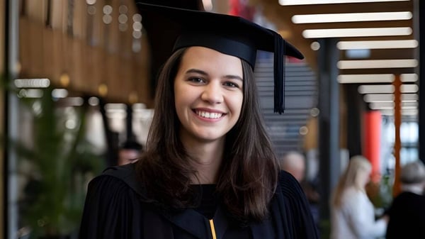 Eine lächelnde Absolventin in schwarzem Talar steht vor einer dekorierten Holzstruktur auf dem Campus der Tauranga Girl´s College.