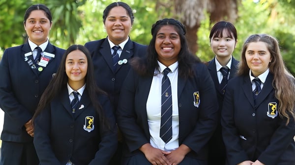 Eine Gruppe von Schülerinnen in Schuluniformen steht gemeinsam in einem grünen Außenbereich des Tauranga Girl´s College.