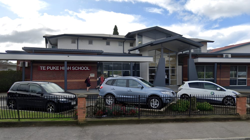 Das moderne Schulgebäude der Te Puke High School mit einem Schild ist von parkenden Autos umgeben.