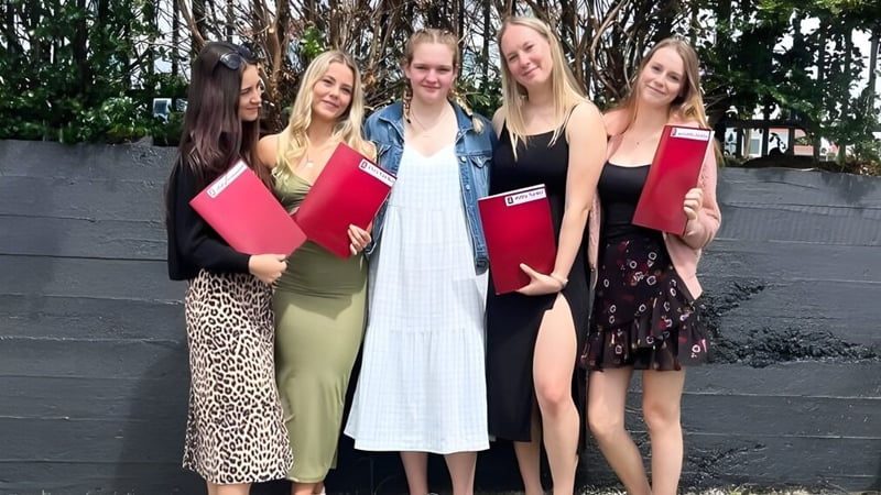 Eine Gruppe junger Schülerinnen steht vor einem Holzzaun im Grünen auf dem Gelände der Te Puke High School.