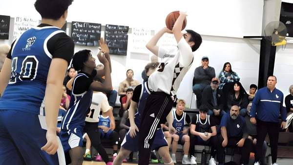 Ein Basketballspiel läuft auf dem Spielfeld der Teays Valley Christian School mit Spielern beider Teams und Zuschauern im Hintergrund.
