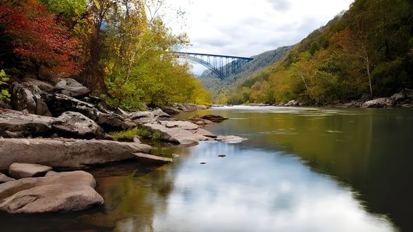 Ein ruhiger Fluss fließt durch eine herbstliche Landschaft mit einer hohen Brücke im Hintergrund auf dem Gelände der Teays Valley Christian School.