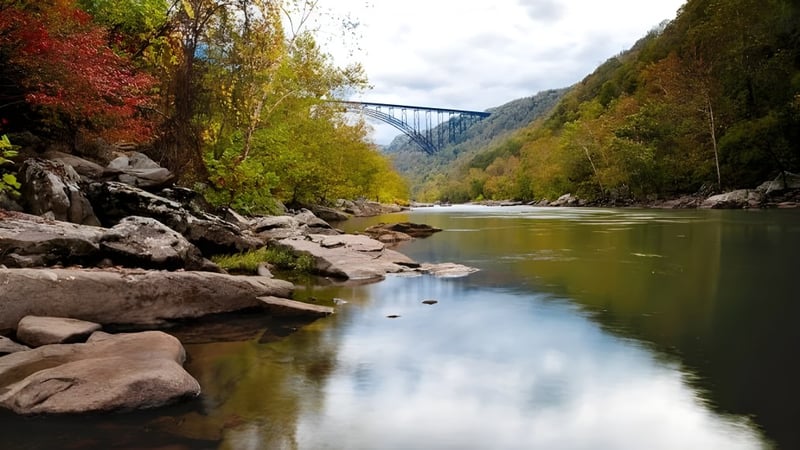 Ein ruhiger Fluss fließt durch eine herbstliche Landschaft mit einer hohen Brücke im Hintergrund auf dem Gelände der Teays Valley Christian School.