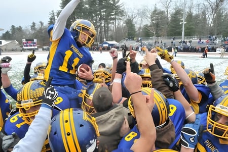 Schüler der Technical Vocational High School feiern gemeinsam auf einem verschneiten Fußballfeld mit Zuschauern im Hintergrund.