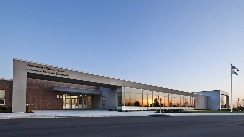 Das moderne Gebäude der Tecumseh Vista Academy mit Glasfront und Ziegelmauerwerk bei klarem Himmel.