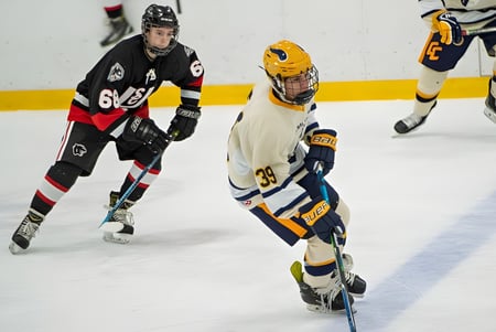 Zwei Hockeyspieler in unterschiedlichen Trikots spielen auf dem Eis der Tecumseh Vista Academy.