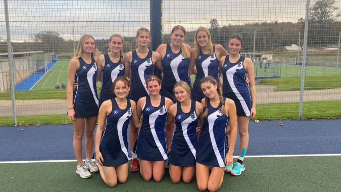 Eine Gruppe junger Athletinnen auf dem Sportplatz des Templemichael College posiert gemeinsam vor einem Zaun und Bäumen.