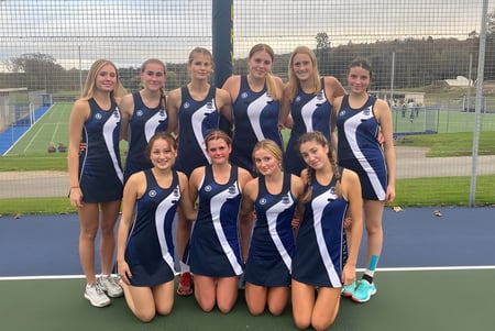 Eine Gruppe junger Sportlerinnen steht gemeinsam auf dem Sportfeld der Templemichael College mit Zaun und Bäumen im Hintergrund.