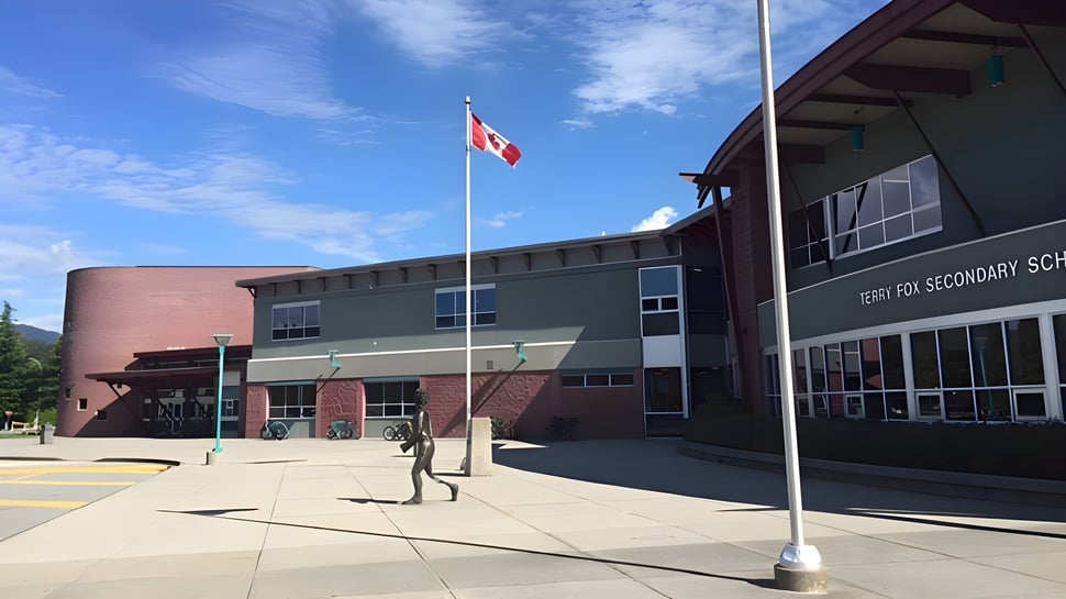 Das mehrstöckige Schulgebäude der Terry Fox Secondary School mit kanadischer Flagge und Personen im Vordergrund.