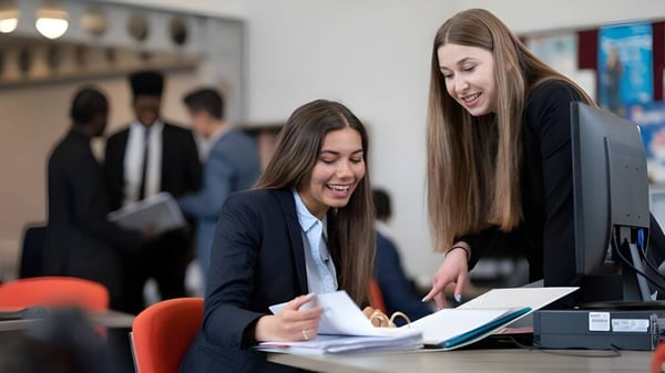 Zwei Schülerinnen des Tettenhall College diskutieren gemeinsam Geschäftsunterlagen in einem professionellen Büro.