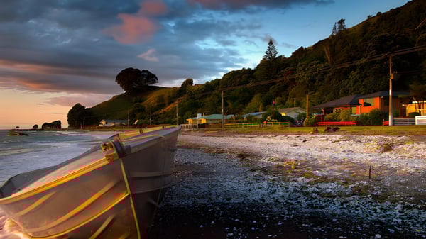 Eine malerische Küstenlandschaft mit Kieselstrand und bunten Häusern bei Sonnenuntergang, nahe der Thames High School.