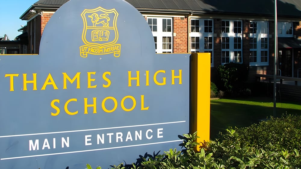 Das große Schild der Thames High School mit dem Wappen vor dem Backsteingebäude und der gestalteten Außenanlage.