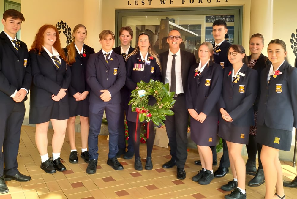 Eine Gruppe Schülerinnen und Schüler der Thames High School steht gemeinsam in einem Flur vor einem Schild mit der Aufschrift ‚Lest We Forget‘.