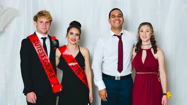 Vier Personen in formeller Kleidung stehen zusammen vor einem weißen Hintergrund auf dem Campus der Thames High School.