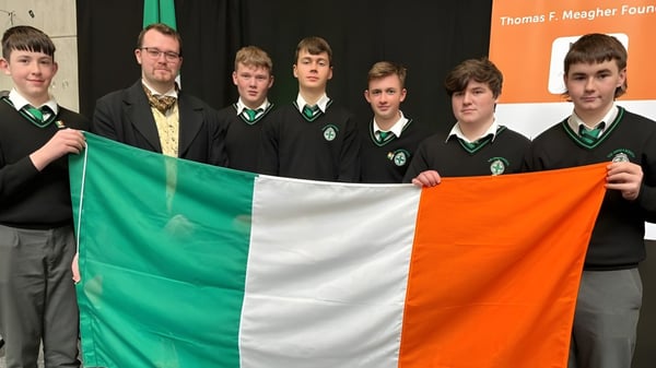Schüler der The Abbey School in Schuluniform halten eine irische Flagge vor einem Banner der Thomas F. Meagher Foundation.