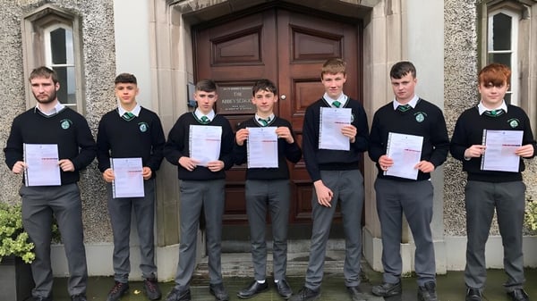 Eine Gruppe von Schülerinnen und Schülern der The Abbey School steht vor einer großen Holztür und hält Zertifikate hoch.