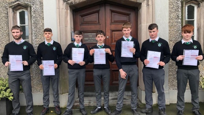 Eine Gruppe Schüler der The Abbey School steht vor einer großen Holztür und hält Zertifikate in den Händen.