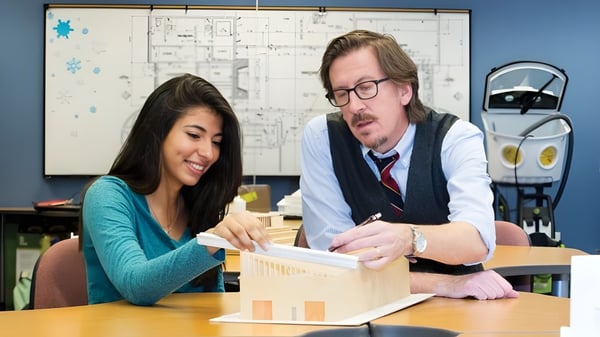 Eine junge Frau und ein älterer Mann führen ein Gespräch an einem Tisch in einem Klassenraum der The Academy MiraCosta.