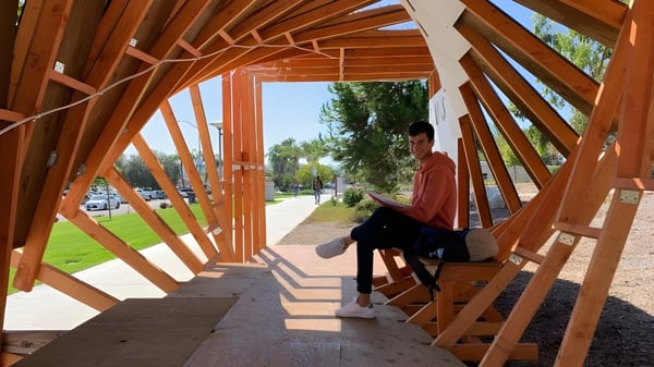 Eine Person sitzt auf einer Bank am Holzweg mit geometrischem Muster auf dem Campus der The Academy MiraCosta.