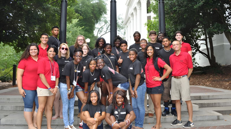 Eine Gruppe von Schülerinnen und Schülern versammelt sich auf Außentreppen vor einem Gebäude mit Säulen auf dem Campus der The Barnes Academy.
