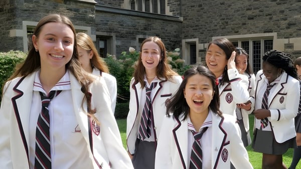Eine Gruppe lächelnder Schülerinnen der The Bishop Strachan School steht vor einem steinernen Gebäude mit Bogenfenstern.