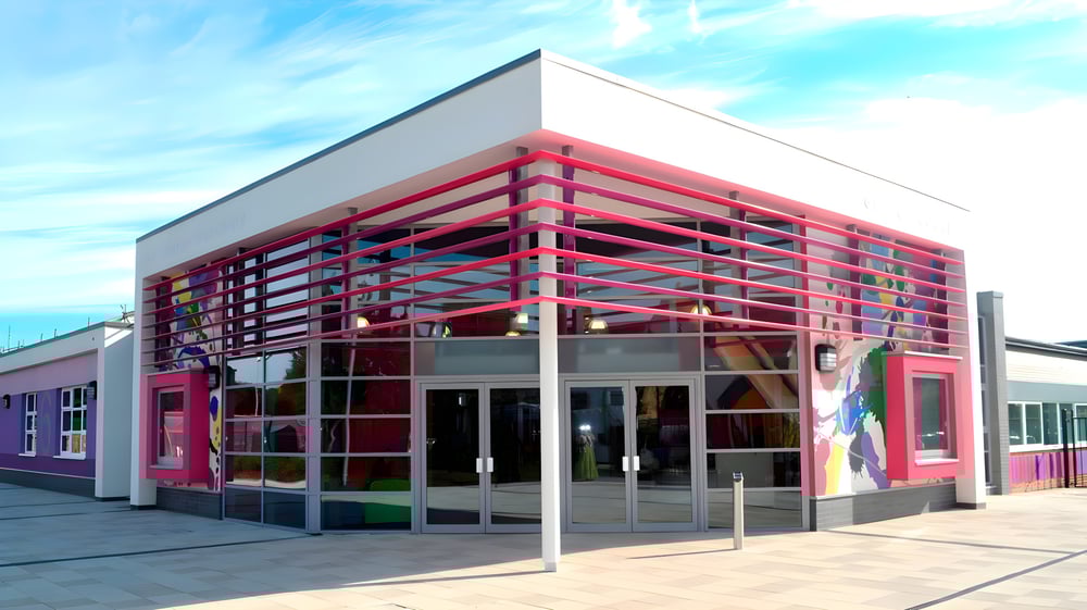 Das moderne, farbenfrohe Gebäude der The Bourne Academy mit markanter geometrischer Gestaltung vor blauem Himmel.