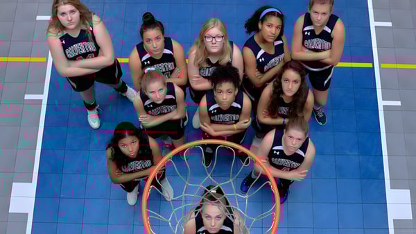 Eine Gruppe junger Basketballspielerinnen steht auf dem Basketballfeld der The Calverton School mit einem Korb im Vordergrund.