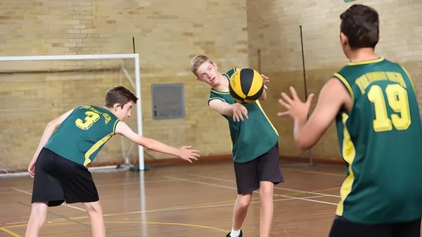 Schüler der The Forest High School spielen Basketball in der Halle, während ein Spieler den Ball zu einem anderen passt.