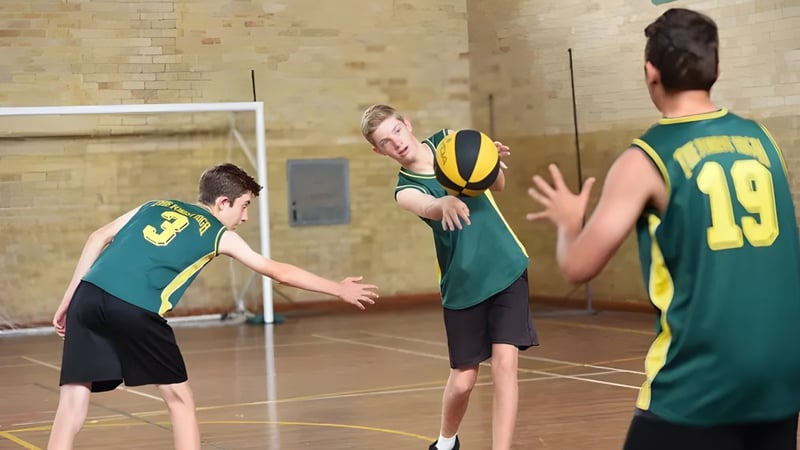 Schüler der The Forest High School spielen Basketball in der Halle, während ein Spieler den Ball zu einem anderen passt.